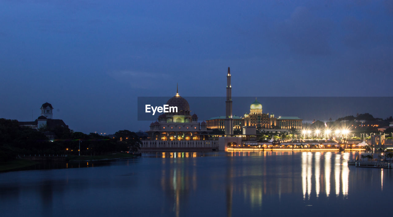 River by illuminated city against clear sky at dusk