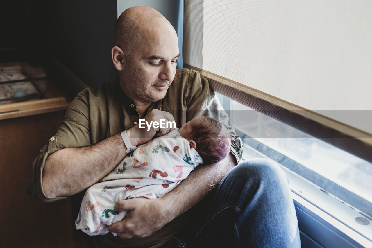 Father holding newborn boy wrapped in blankets in hospital