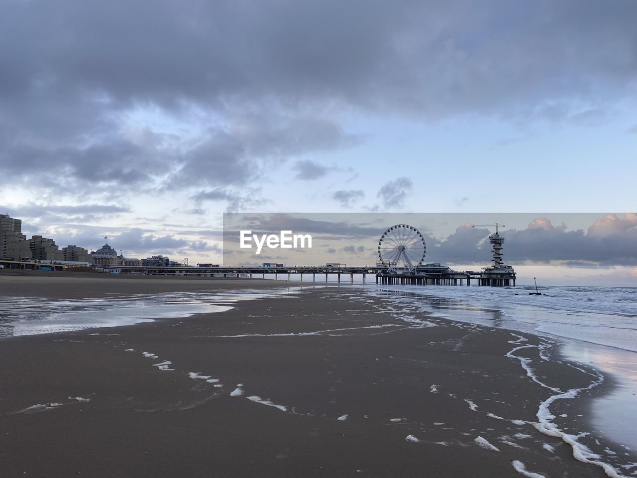 View of ferris wheel at beach against cloudy sky
