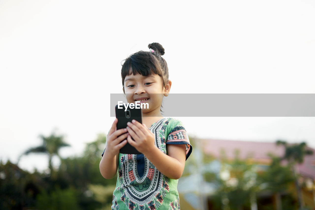 Girl using phone against sky