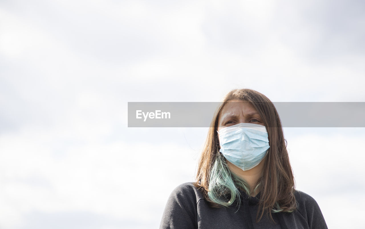 Low angle view of woman wearing mask standing against fence