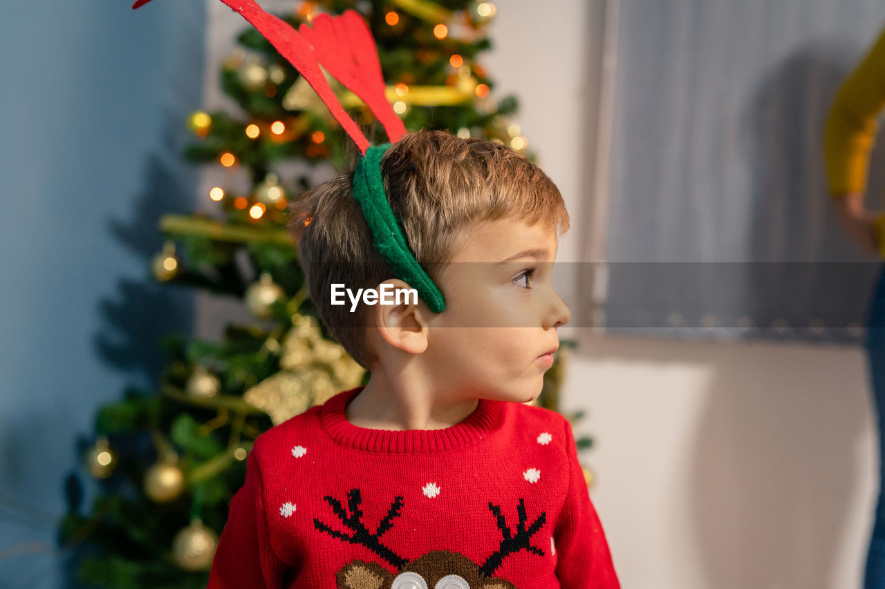 Cute boy standing against christmas tree at home