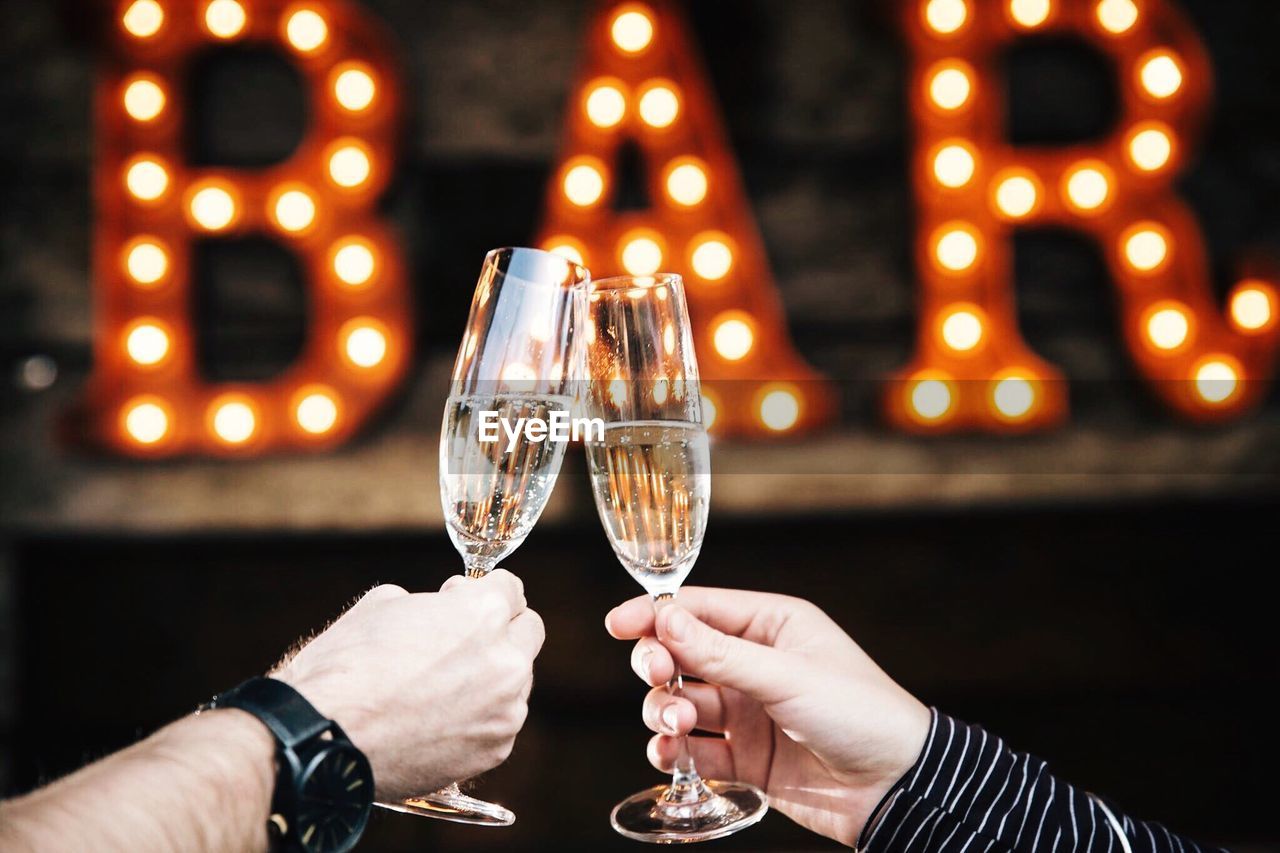 Cropped image of hands toasting champagne flutes in bar
