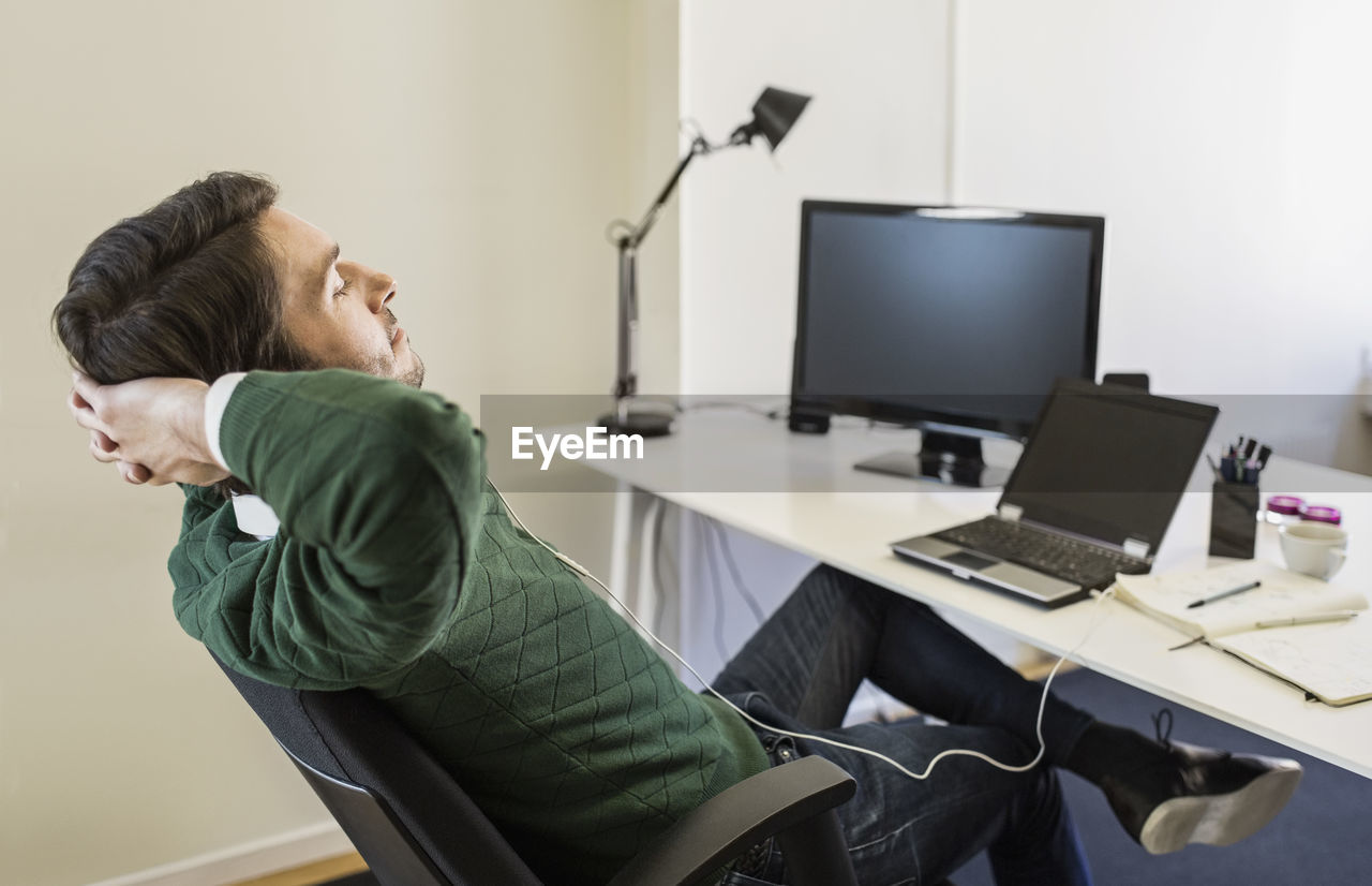 Businessman with hands behind head relaxing at desk in office