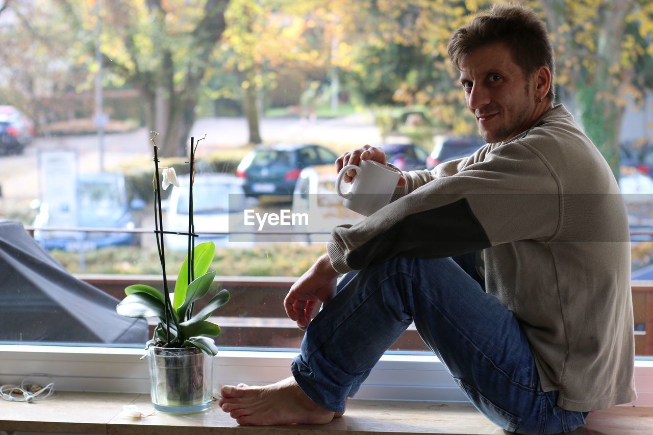 Portrait of man drinking coffee while sitting at window