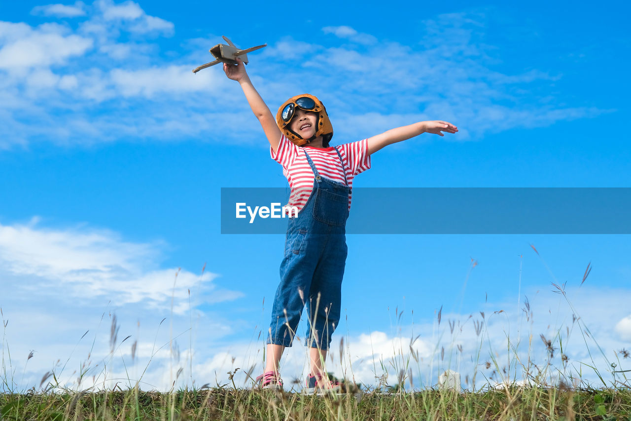 Rear view of woman with arms outstretched standing on field against sky