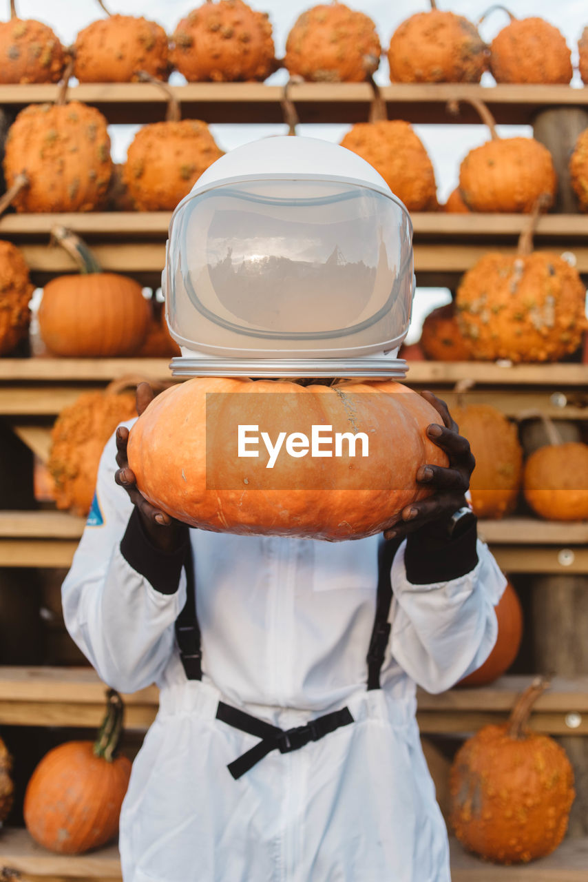 Person wearing spacesuit while holding pumpkin in store