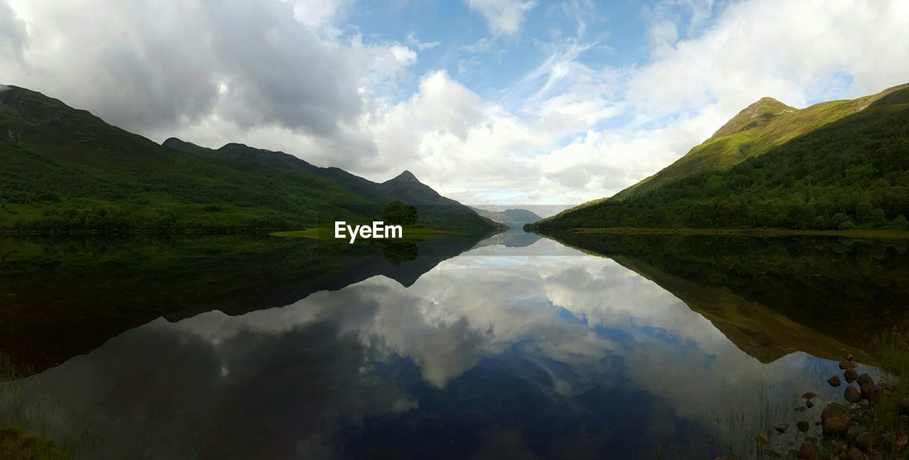 Symmetrical view of mountains and clouds reflecting in lake