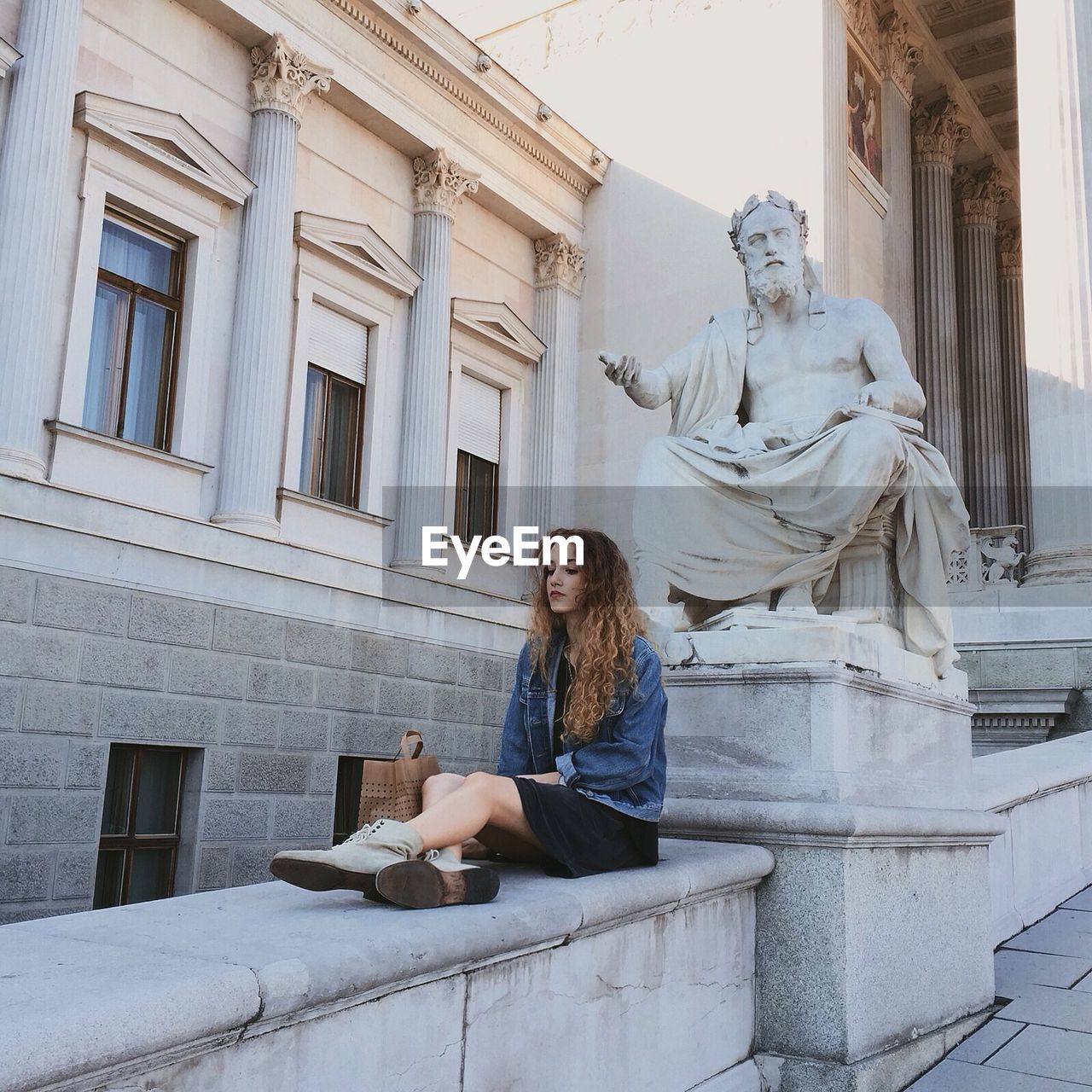 Full length of beautiful woman sitting by statue against historic building