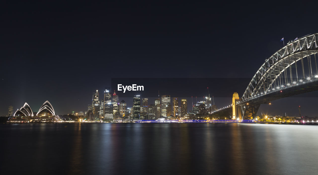 Illuminated sydney harbour bridge and opera house by bay against clear sky