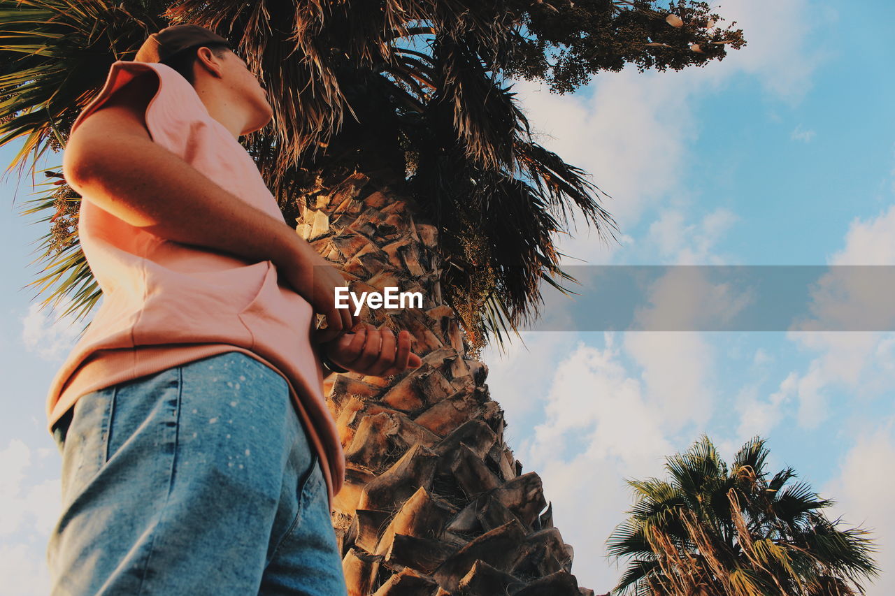 Low angle view of woman standing by tree against sky