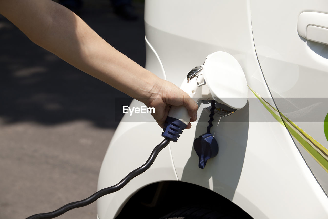 Cropped hand charging car at station