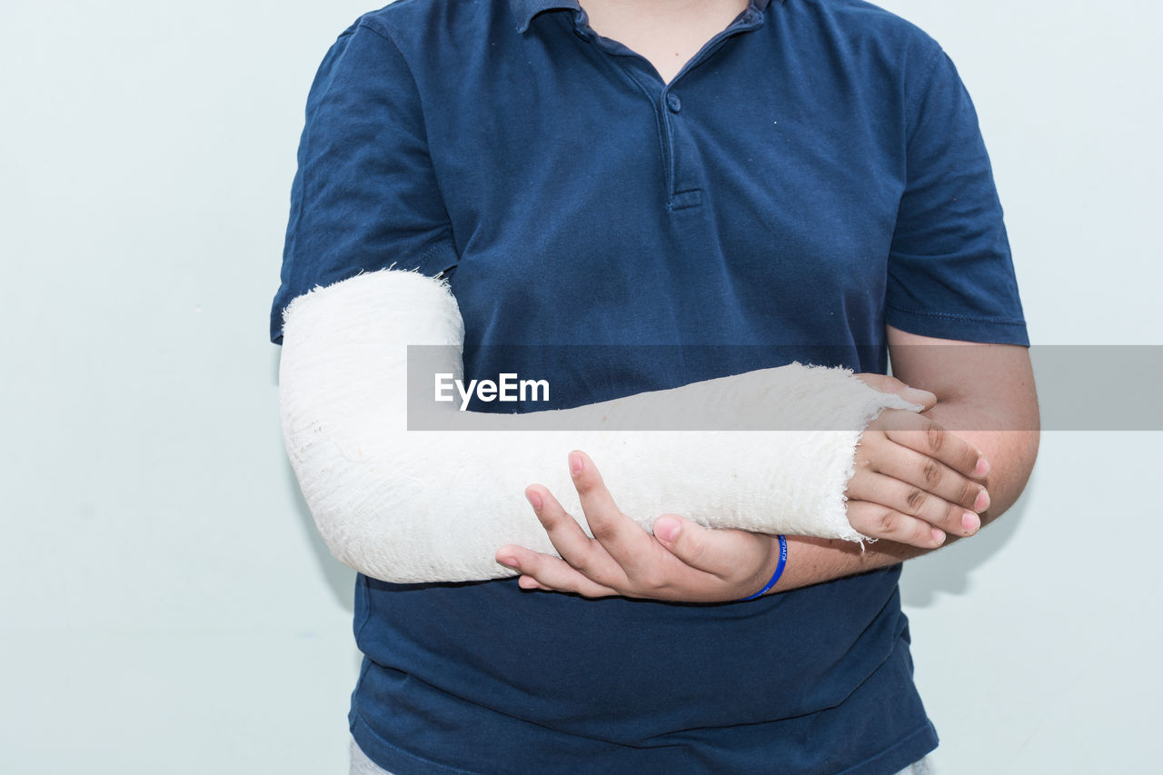 Midsection of boy with fractured hand standing against white background