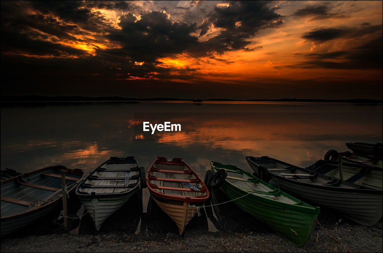 Boats moored on lakeshore against sky during sunset