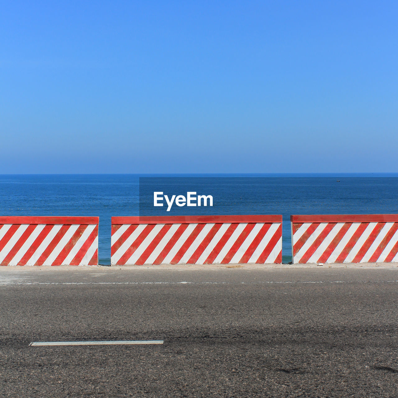 Striped retaining wall on road by sea against clear sky