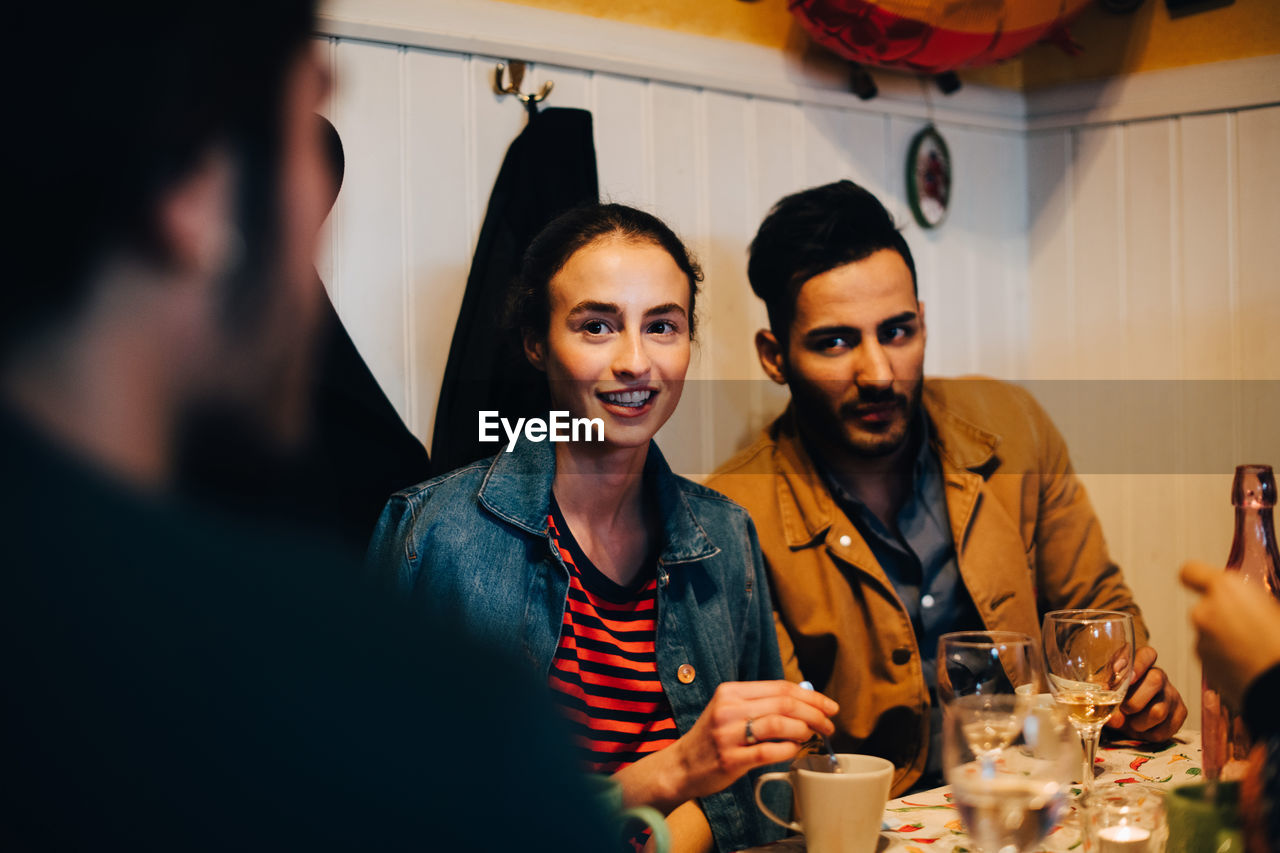 Young man and woman looking at male friend during dinner party at restaurant