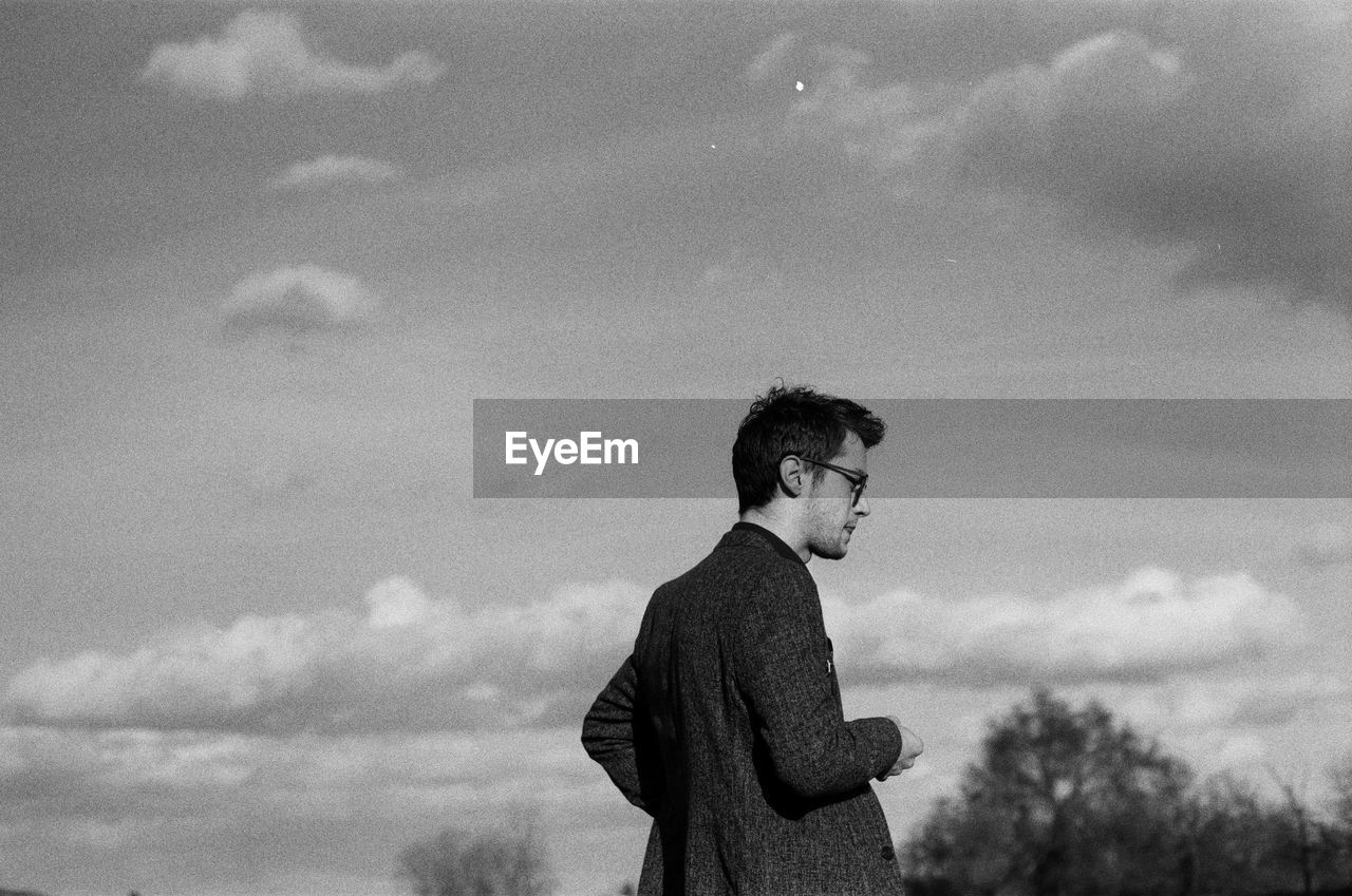 Side view of young man looking away against sky