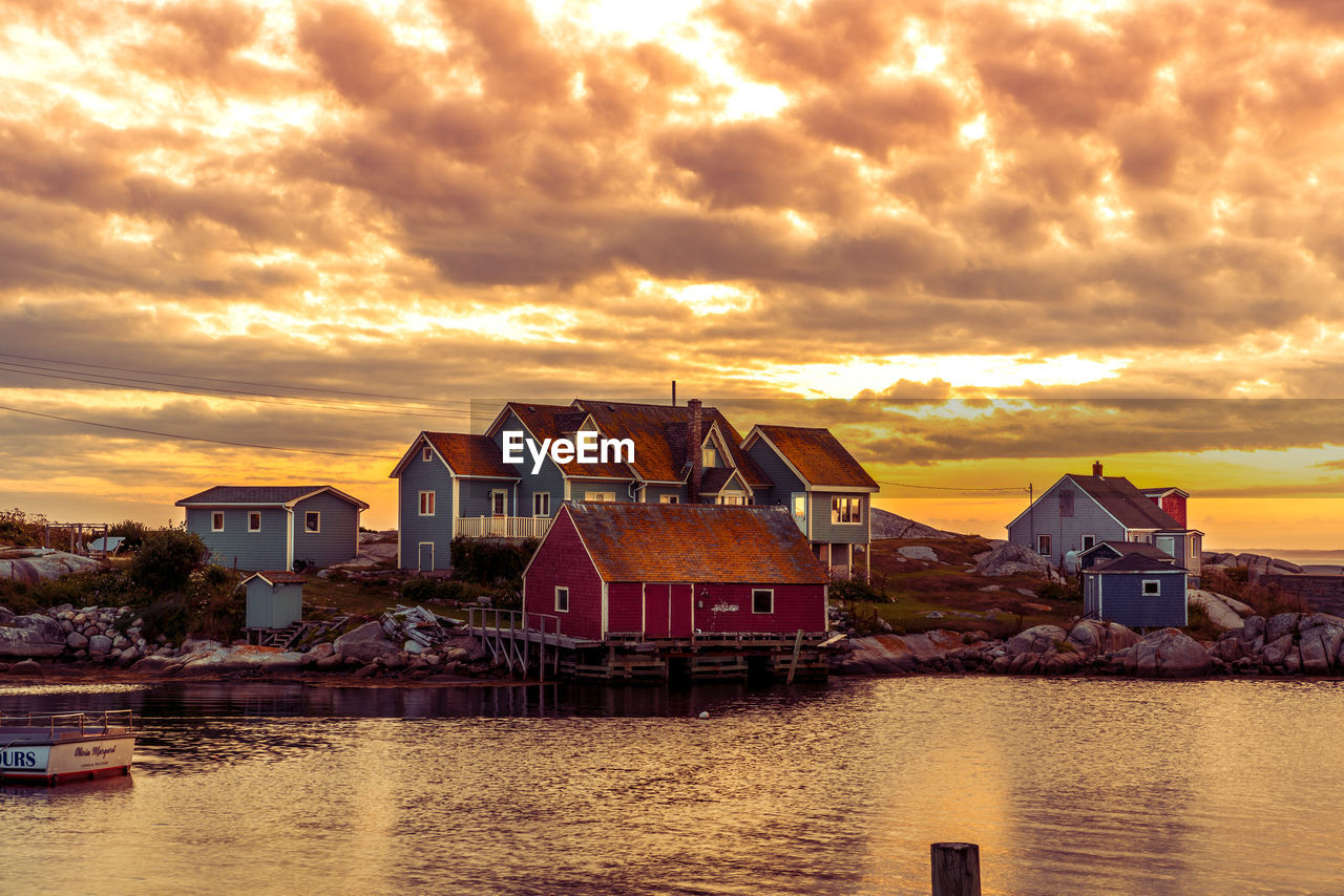 BUILDINGS BY RIVER AGAINST SKY AT SUNSET