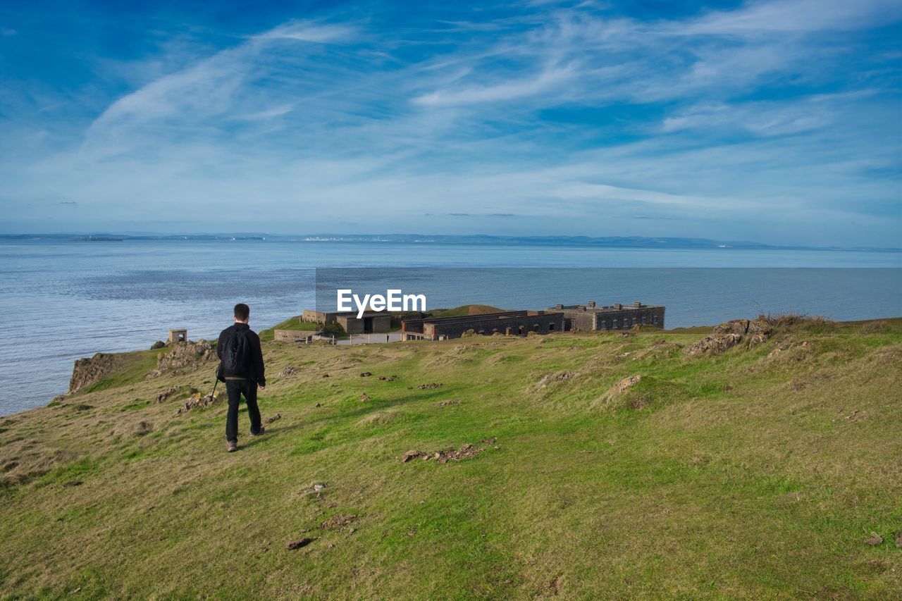 Rear view of men on field by sea against sky