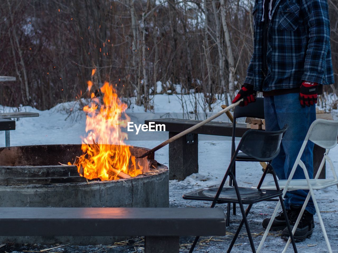 Man standing with stick by fire during winter