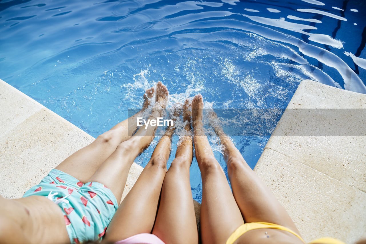Legs of friends splashing in pool