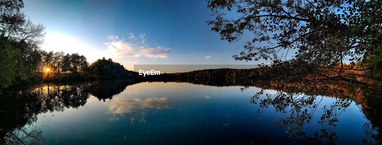 REFLECTION OF SILHOUETTE TREES IN LAKE AGAINST SKY