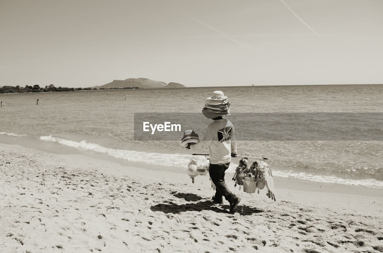 Rear view full length of vendor with hats walking on shore at beach