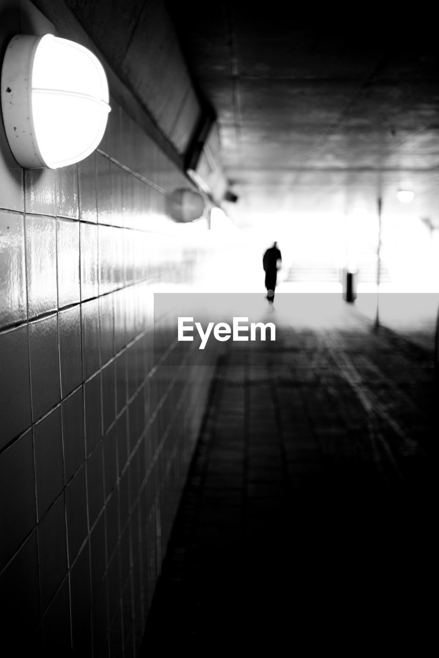 Silhouette man walking in illuminated underpass