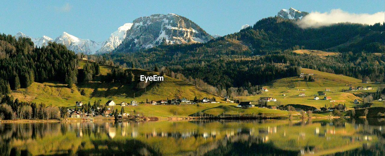 PANORAMIC VIEW OF TOWNSCAPE BY LAKE AGAINST MOUNTAIN