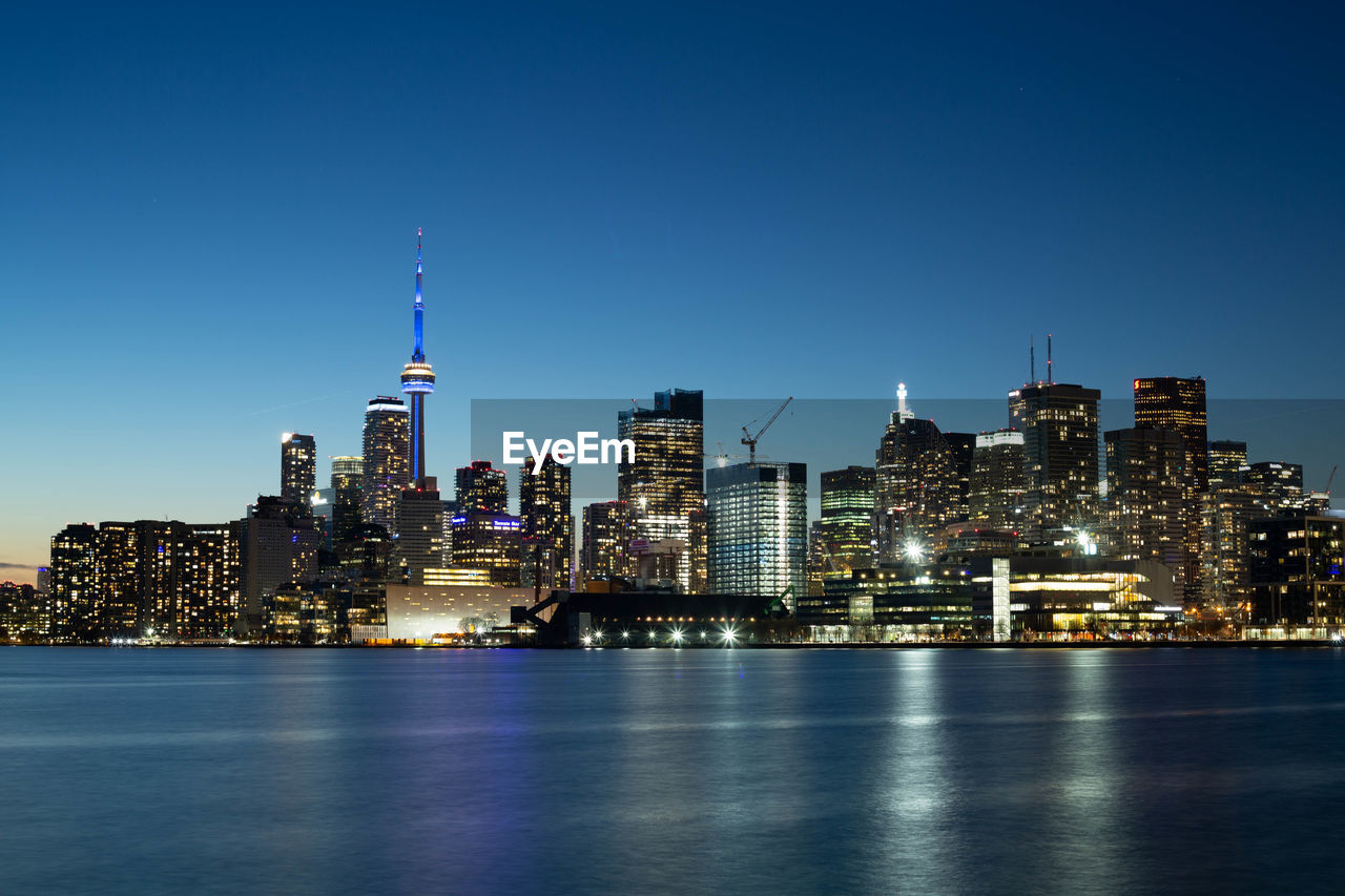 Illuminated buildings in city against clear sky evening 