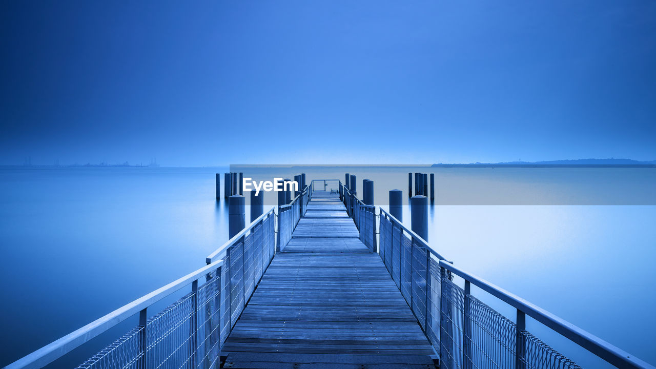 Pier on sea against clear blue sky