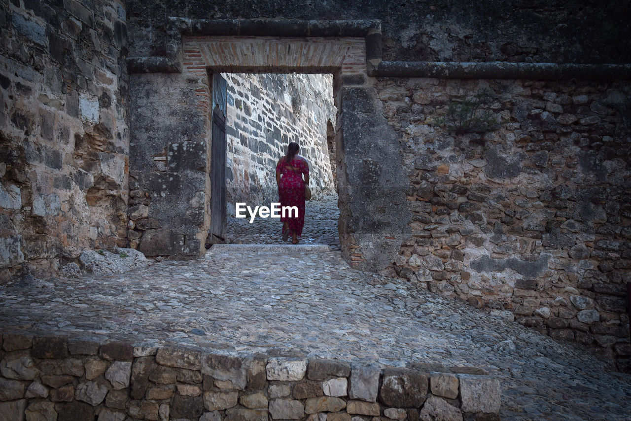 REAR VIEW OF WOMAN STANDING IN OLD RUIN