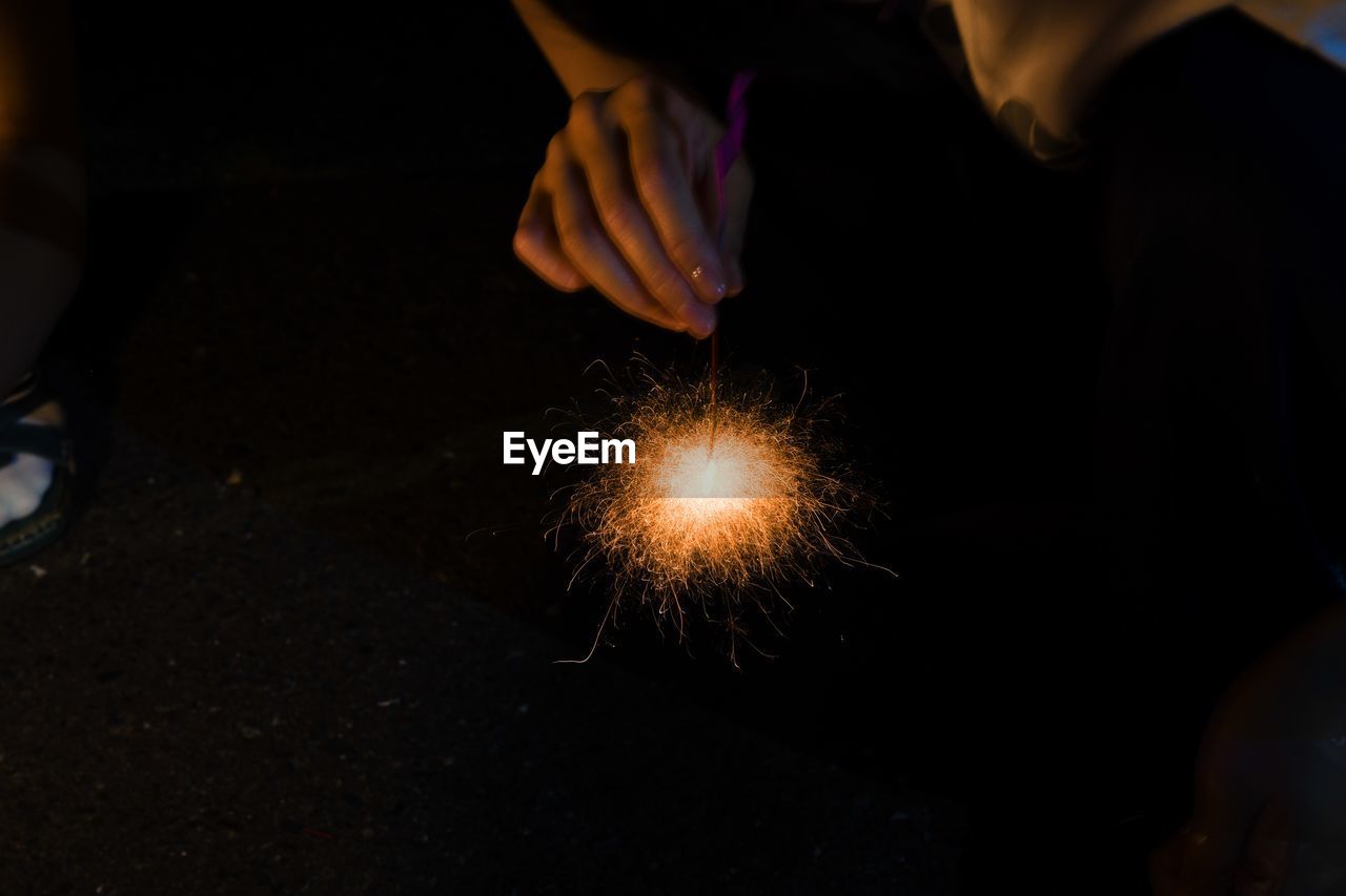 Cropped hand of woman holding sparkler against sky at night