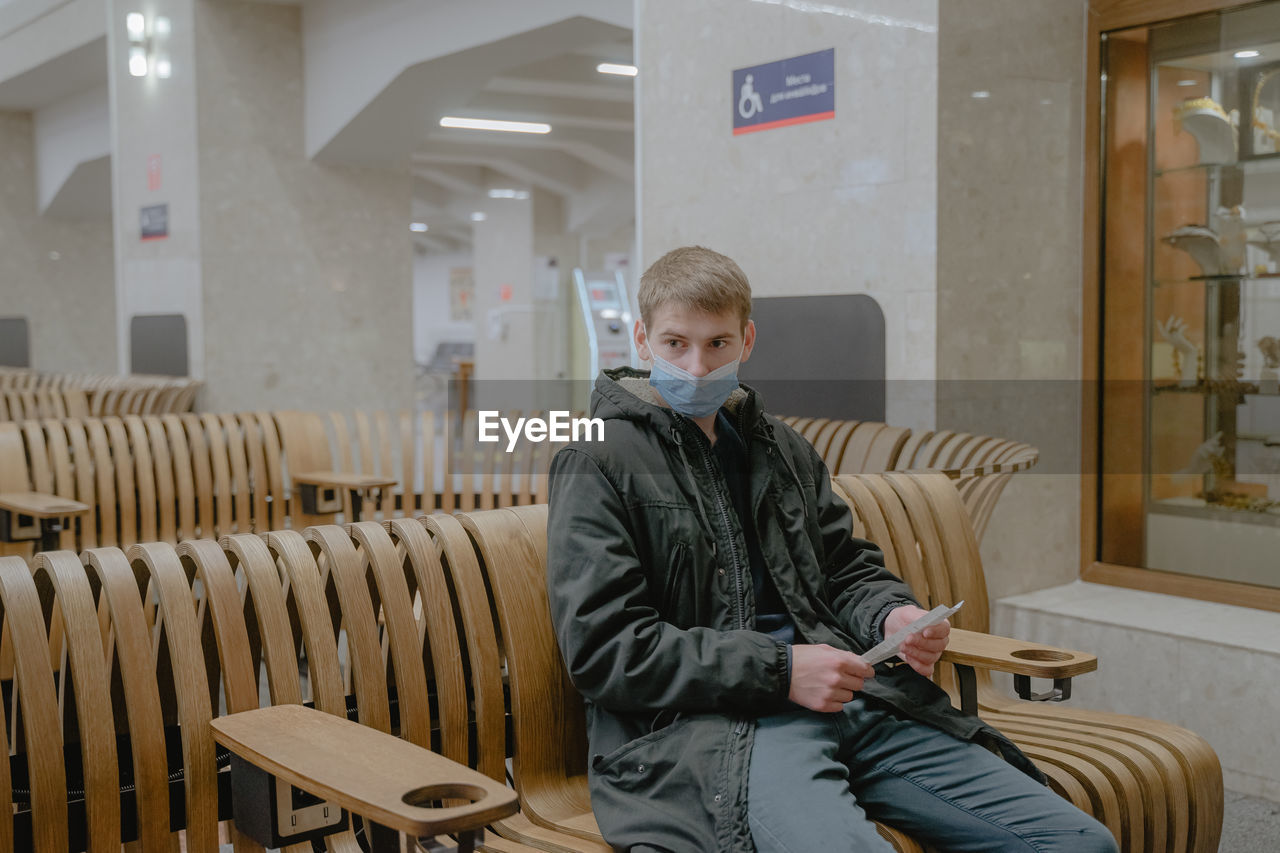 Sitting waiting for the train to leave, with a thoughtful look, a guy in a medical mask, in a public