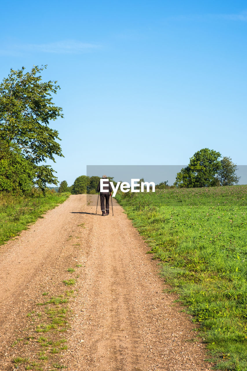 Elderly woman walking with rods on a dirt road