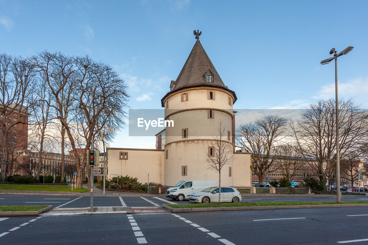 architecture, building exterior, built structure, sky, road, tree, building, city, street, transportation, nature, bare tree, place of worship, tower, plant, day, downtown, road marking, no people, symbol, marking, travel destinations, outdoors, sign, landmark, town, mode of transportation, the past, history, blue, motor vehicle, clear sky, car