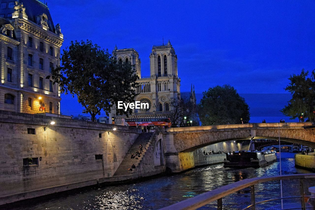 Illuminated bridge by river against blue sky at night