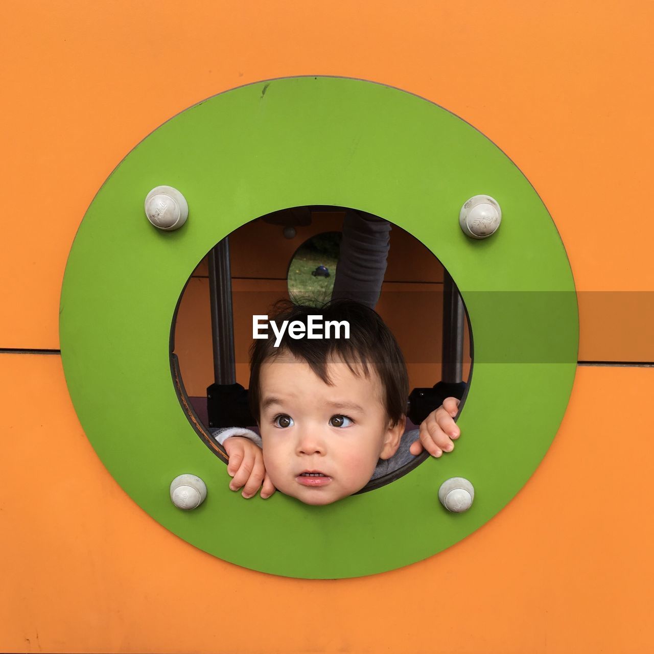 Cute baby boy looking through window of jungle gym in playground