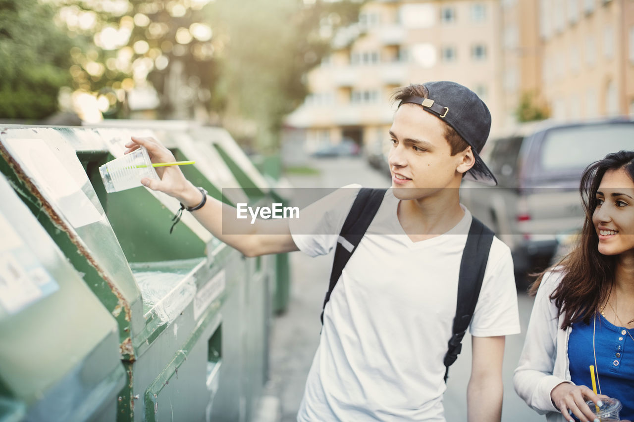 Teenager putting disposable glass in garbage bin on street