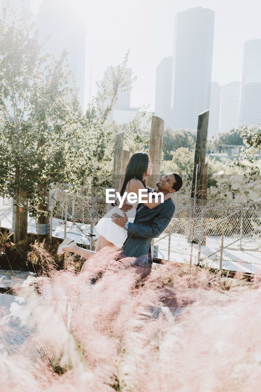 Couple embracing by fence against trees