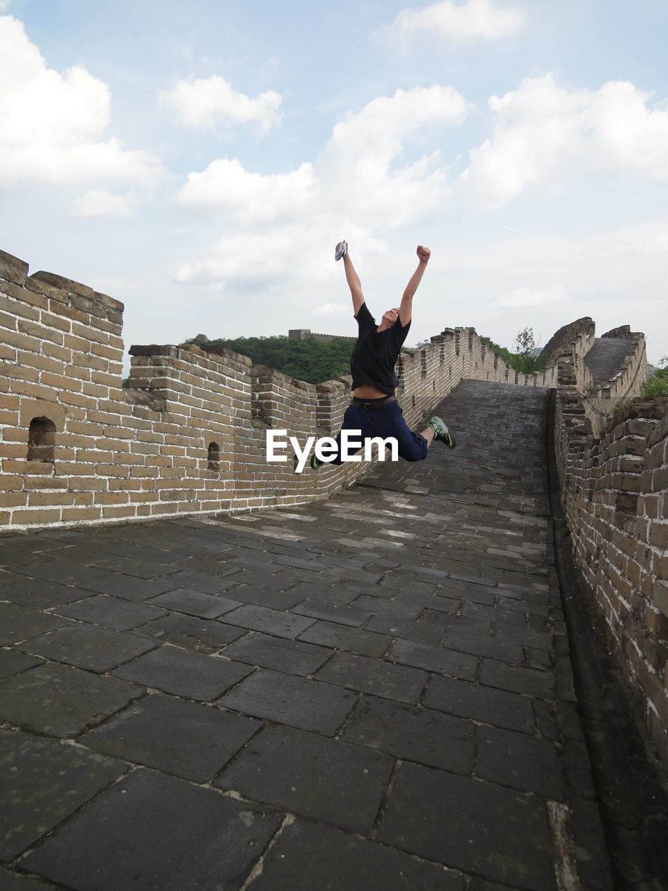 Full length of cheerful woman jumping on great wall of china against sky
