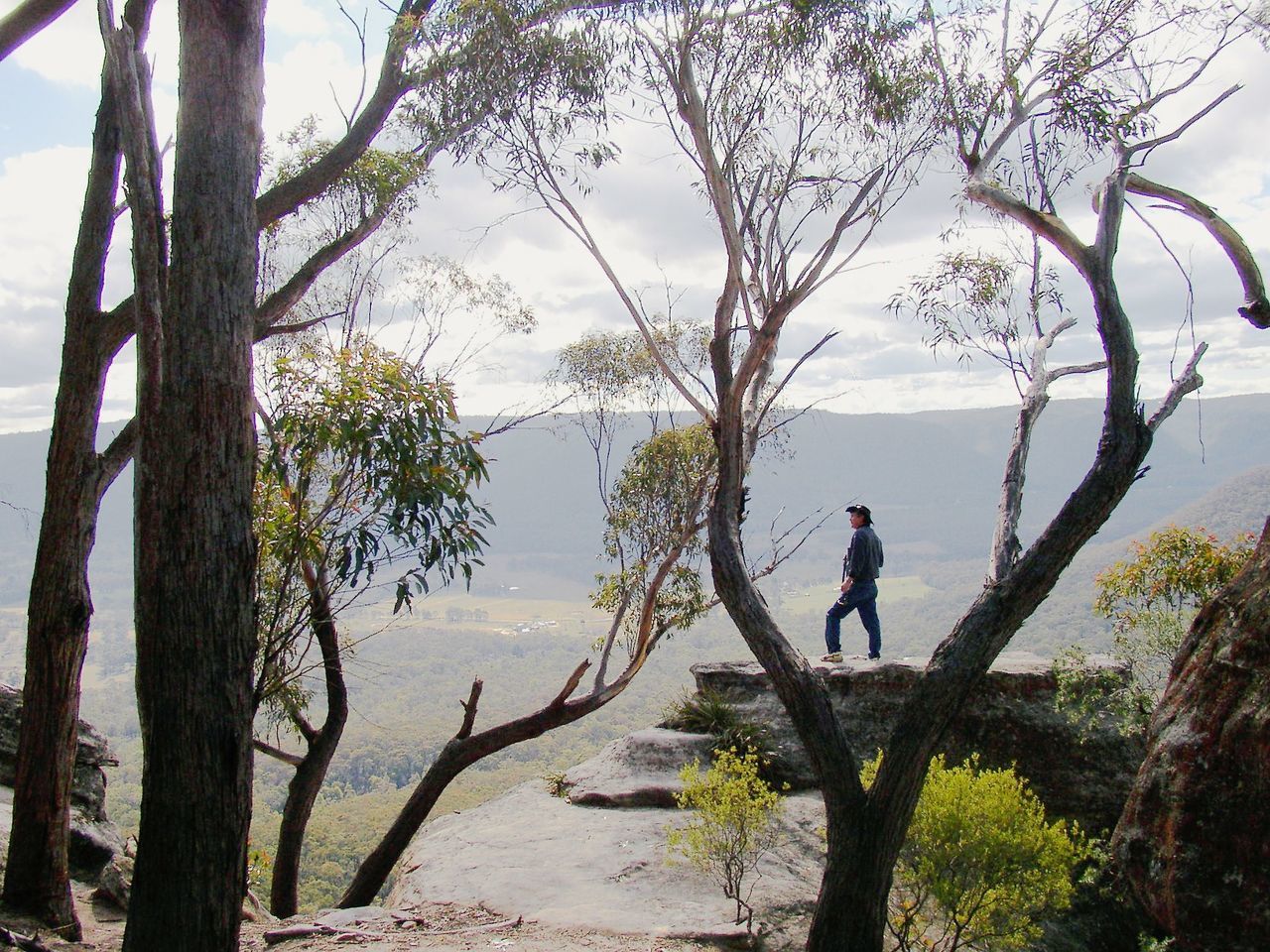 Man standing on cliff by mountains against sky