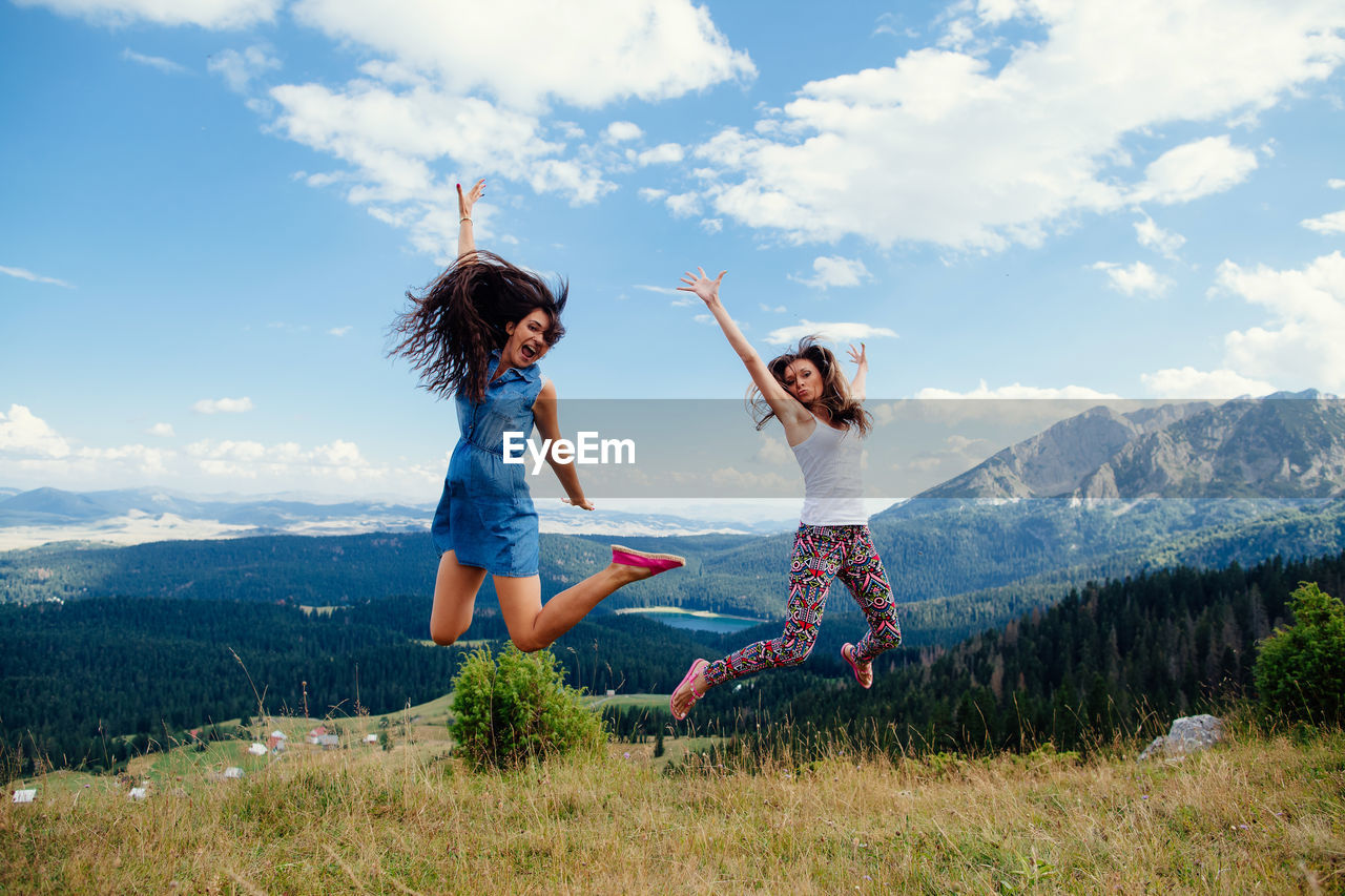 Full length of happy friends jumping over landscape against sky