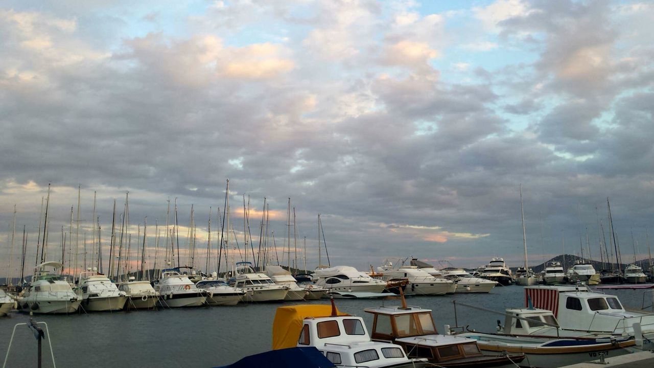 SAILBOATS MOORED ON HARBOR AGAINST SKY