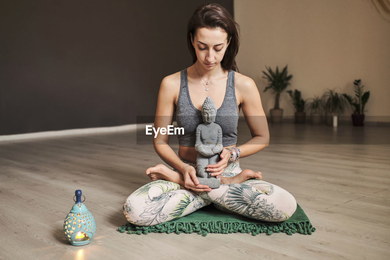 Young woman meditates alone in yoga studio with aroma lamp and budda