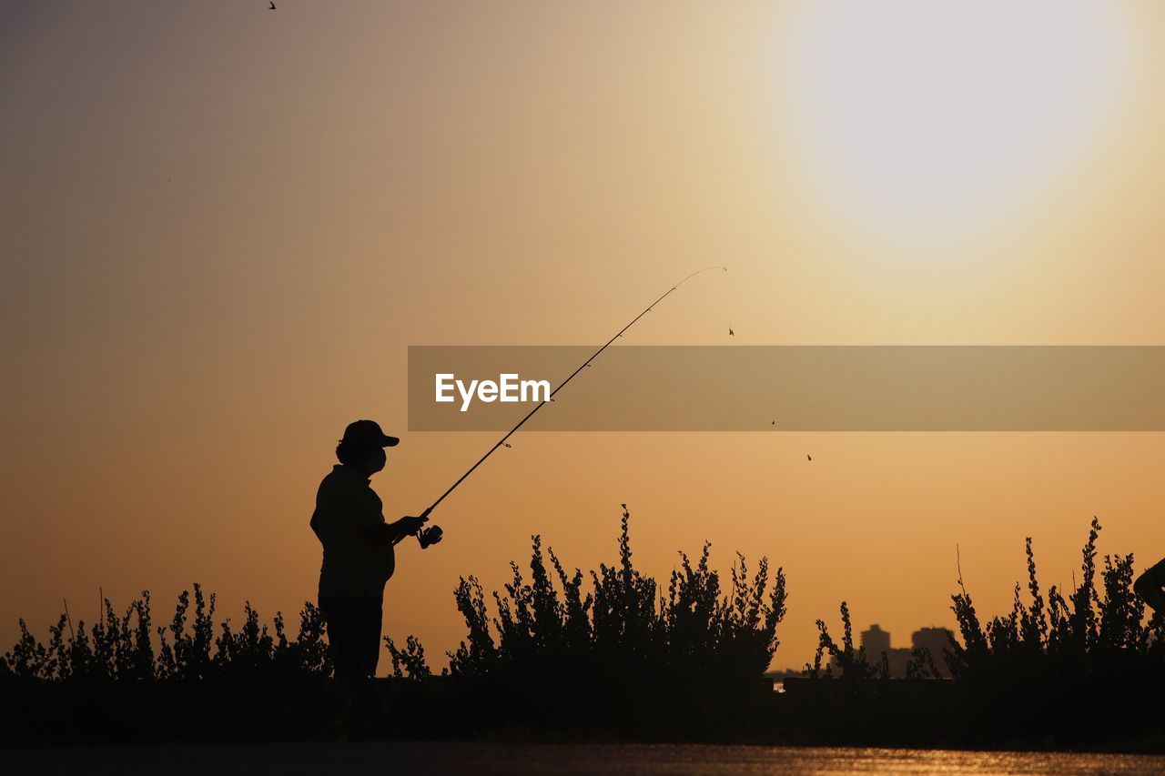 Silhouette man fishing at sunset