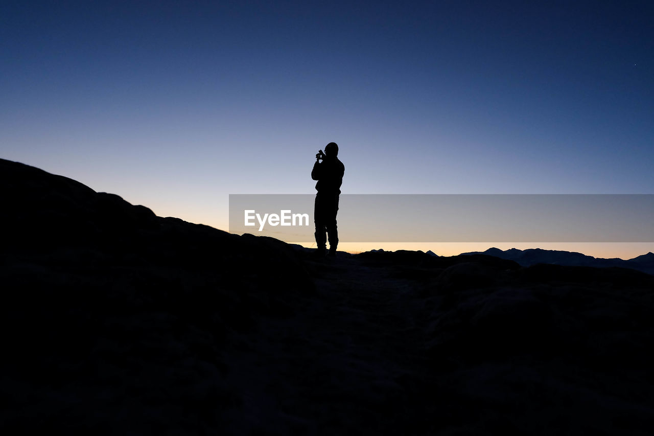 Silhouette man standing on hill against clear sky at dusk