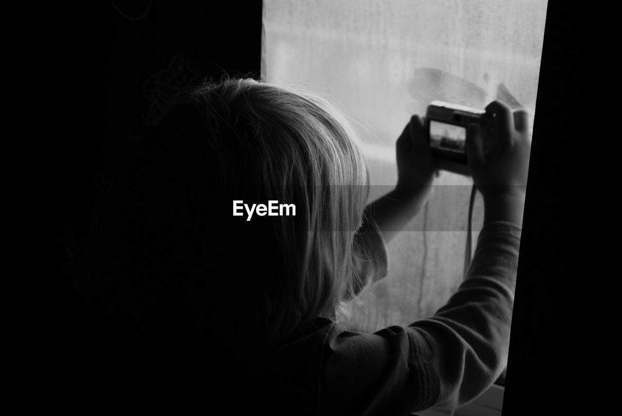 Rear view of boy photographing through window