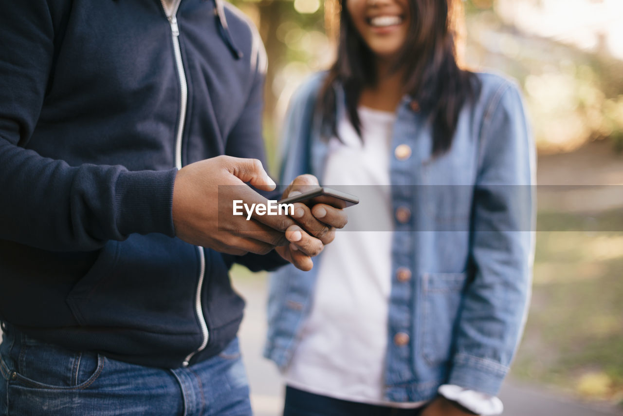 Midsection of man using mobile phone while standing by female friend