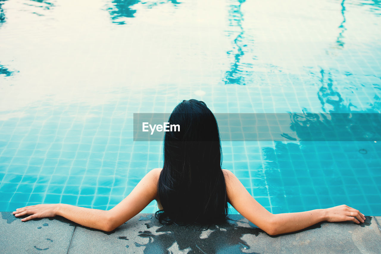 Rear view of woman leaning at poolside